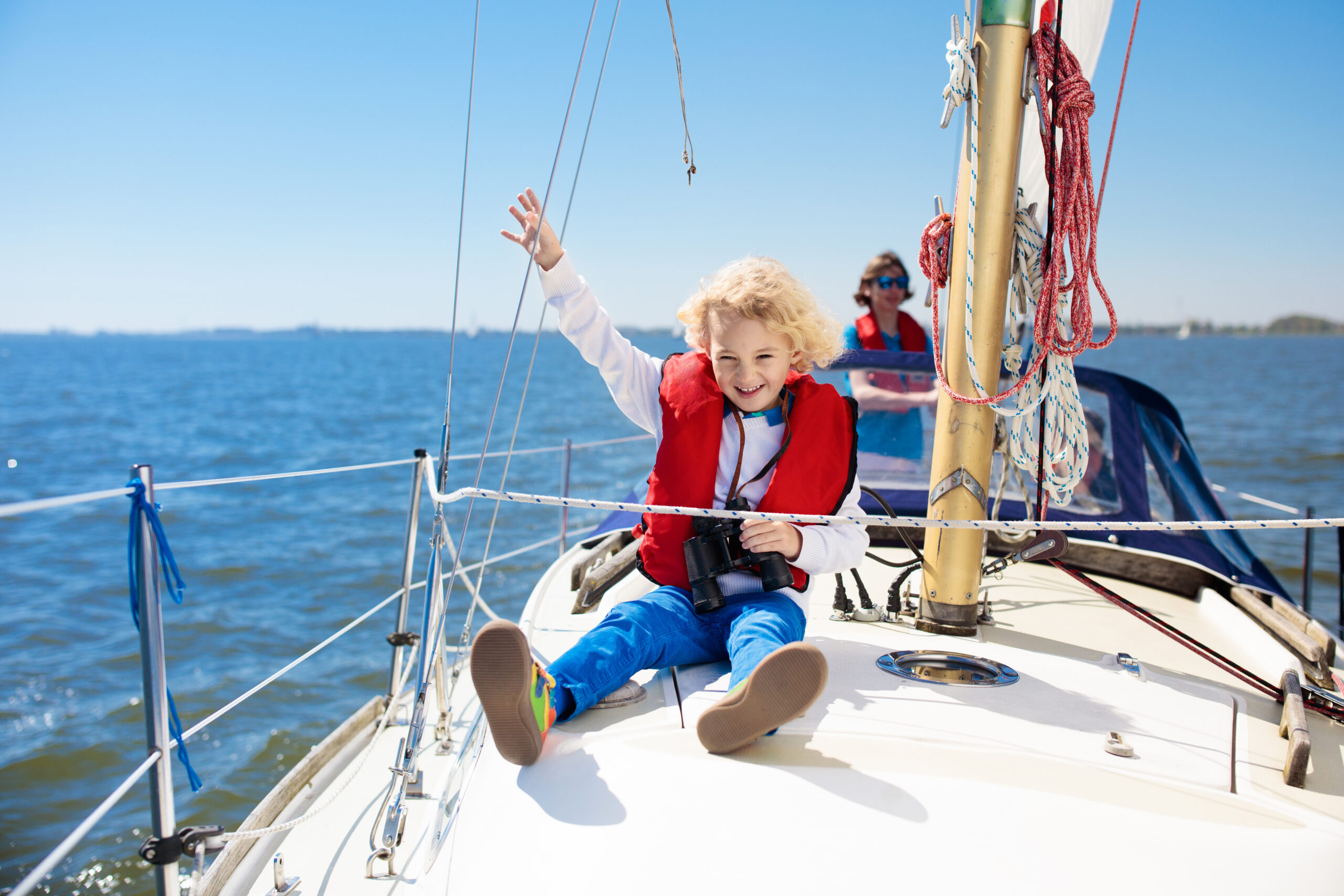 little kid on a sail boat wearing jeans, a shirts, and vest