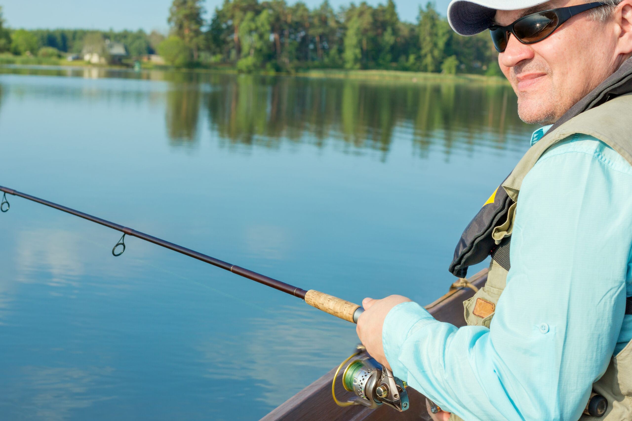 Man fishing from a boat, wearing a hat, sunglasses, sun shirt, and vest.